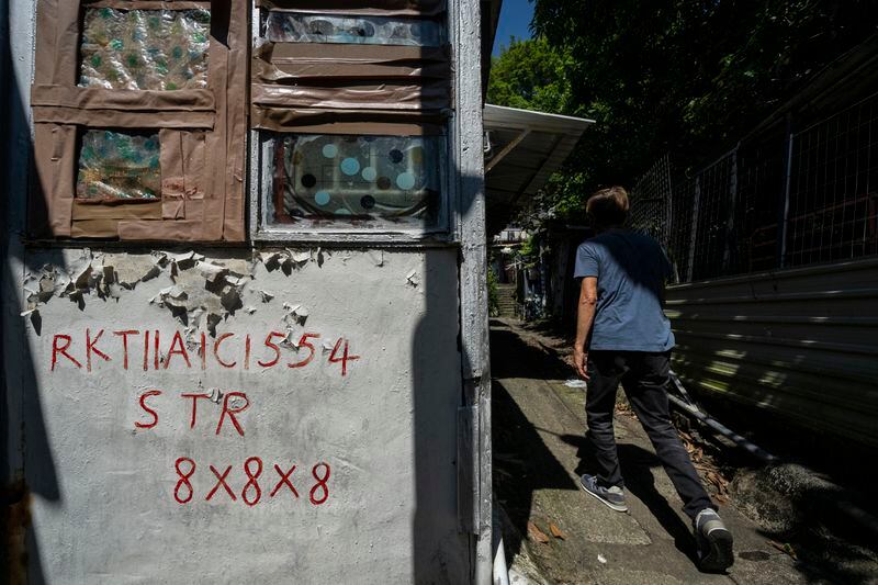 Villager Lo Yuet-ping walks past squatter registration info written on the walls of a house in Cha Kwo Ling village in east Kowloon, Hong Kong, Sunday, Aug. 25, 2024. (AP Photo/Chan Long Hei)