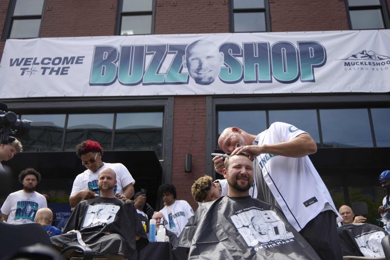 Seattle Mariners catcher Cal Raleigh has his head shaved by former Mariners player Jay Buhner on Buhner Buzz Night, Thursday, June 13, 2024, in Seattle. The promotion is based on Buhner's shaved-head style. (AP Photo/John Froschauer)