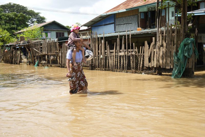 A women and child wade through a flooded road, in Naypyitaw, Myanmar, Myanmar, Tuesday, Sept. 17, 2024. (AP Photo/Aung Shine Oo)