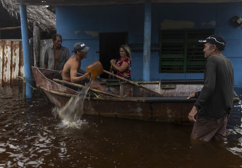 A man removes water from a boat while talking to neighbors after the passage of Hurricane Helene in Guanimar, Artemisa province, Cuba, Wednesday, Sept. 25, 2024. (AP Photo/Ramon Espinosa)