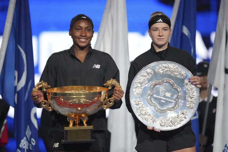 Coco Gauff of the United States, left, holds the championship trophy as she pose for photographers with Karolina Muchova of Czech Republic after defeating her in the women's singles final match at the China Open tennis tournament at the National Tennis Center in Beijing, Sunday, Oct. 6, 2024. (AP Photo/Achmad Ibrahim)