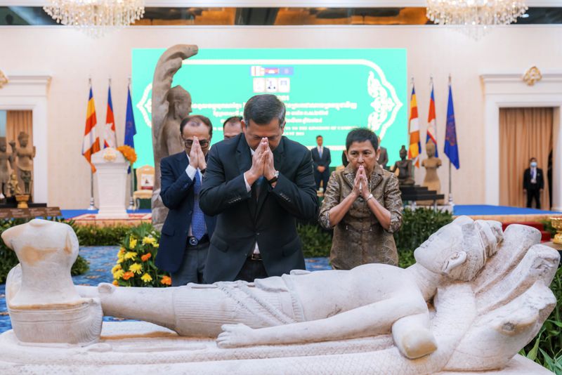 In this photo released by Agence Kampuchea Press (AKP), Cambodian Prime Minister Hun Manet, front, prays before a statue with Culture and Fine Arts Phoeurng Sackona, right, during a ceremony for the return of artifacts in Peace Palace in Phnom Penh, Cambodia, Thursday, Aug. 22, 2024. (AKP via AP)