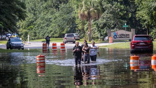 A group of people walk through a flooded road on Bradley Boulevard on Monday in Savannah. (AJC Photo/Katelyn Myrick)