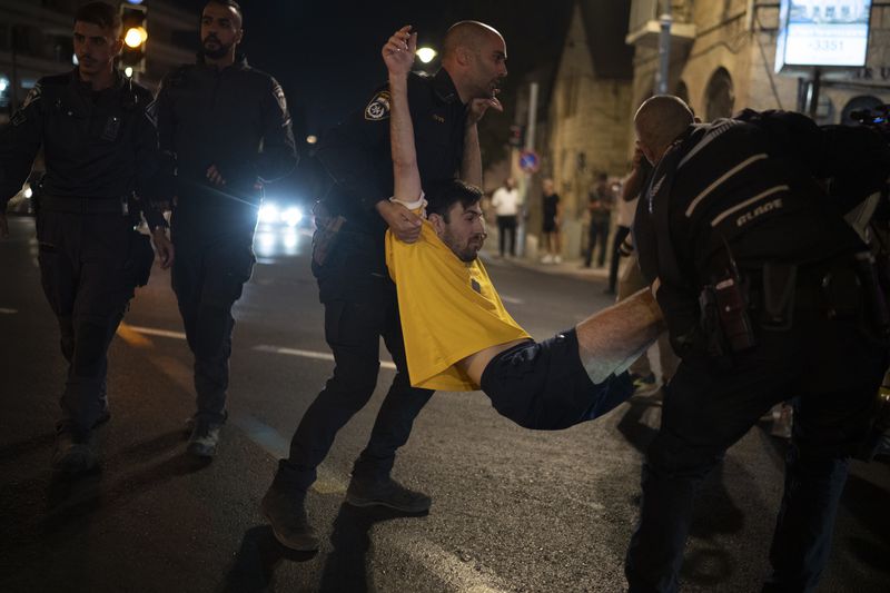 Israeli police officers move a demonstrator blocking a street during a protest, in Jerusalem, Tuesday, Aug. 20, 2024. People gather to honor the memories of six men whose bodies were returned and to call for a deal to release the remaining captives. (AP Photo/Leo Correa)