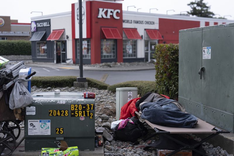 A person leaves a KFC restaurant as an unhoused person sleeps at the busy intersection of Oregon Coast Highway and 5th Street on June 19, 2024, in Brookings, Ore. The Supreme Court on Friday, June 28, allowed cities to enforce bans on homeless people sleeping outside in public places, ruling along ideological lines that such laws don't amount to cruel and unusual punishment, even in West Coast areas where shelter space is lacking. (AP Photo/Jenny Kane)