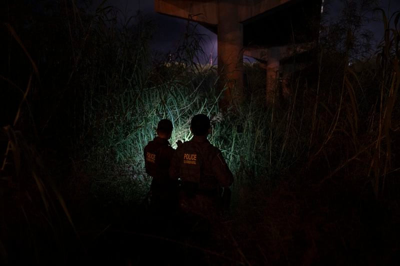 Andrés García, left, and Christina Smallwood, Border Patrol agents and Public Affairs officers, look for migrants underneath the vehicular McAllen-Hidalgo International Bridge in Hidalgo, Texas, early Friday, Aug. 9, 2024. (Verónica Gabriela Cárdenas/The Texas Tribune via AP)