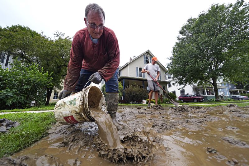 John Companion, left, dumps a bucket of muddy water while helping his friend Scott Mackie, right, clear his flooded basement while cleaning up the remnants of Hurricane Beryl, Thursday, July 11, 2024, in Waterbury, Vt. Mackie said his basement was filled with nearly five feet of muddy mixture, which friends and neighbors are helping to empty. (AP Photo/Charles Krupa)
