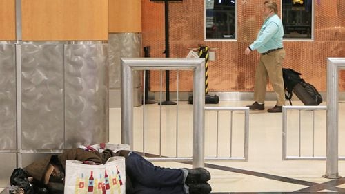 A man (left) sleeps on the ground in the domestic terminal of Hartsfield-Jackson International Airport as flight passengers (right) walk toward security on Friday, February 7, 2020, in Atlanta. Many of Atlanta’s homeless sleep overnight in the airport’s domestic terminal when the city experiences frigid winter temperatures. The man (left) wished not to be identified. (Christina Matacotta/crmatacotta@gmail.com)