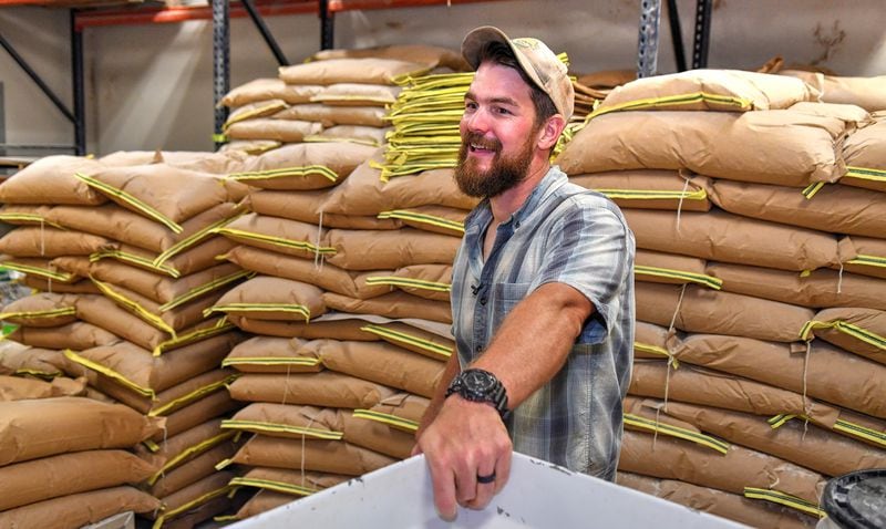 Nathan Brett, co-owner of DaySpring Farms just outside Danielsville, stands in the milling room in front of stacks of 50-pound bags of finished products ready for sales. DaySpring Farms is an organic certified farm that grows, harvests and mills grains on-site. (Chris Hunt for The Atlanta Journal-Constitution)