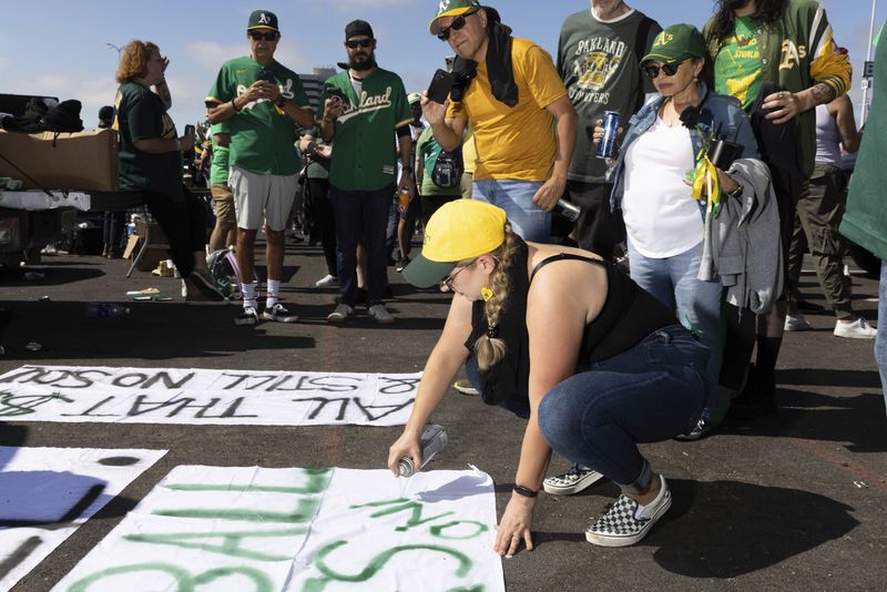 Michelle Leon paints a sign outside the Oakland Coliseum before a baseball game between the Oakland Athletics and the Texas Rangers Thursday, Sept. 26, 2024, in Oakland, Calif. (AP Photo/Benjamin Fanjoy)