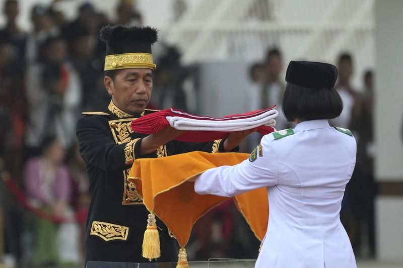 Indonesian President Joko Widodo, left, hands national Red-White flag to a bearer to be hoisted during the ceremony marking Indonesia's 79th anniversary of independence at the new presidential palace in its future capital of Nusantara, a city still under construction on the island of Borneo, Saturday, Aug. 17, 2024. (AP Photo/Achmad Ibrahim)