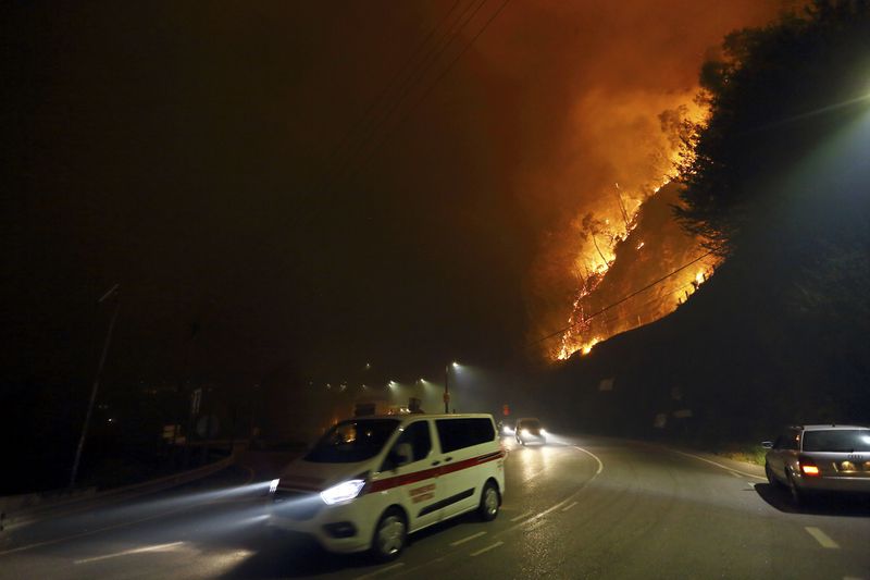 Vehicles drive past a fire burning by the road near Sever do Vouga, a town in northern Portugal that has been surrounded by forest fires, Monday night, Sept. 16, 2024. (AP Photo/Bruno Fonseca)