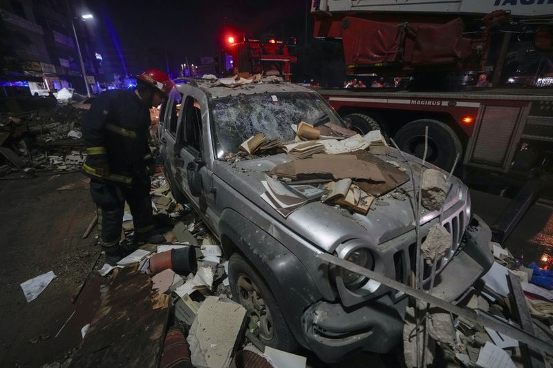 A firefighter inspects a damaged car near a building that was hit in an Israeli airstrike, in Beirut, Lebanon, early Monday, Sept. 30, 2024. (AP Photo/Bilal Hussein)