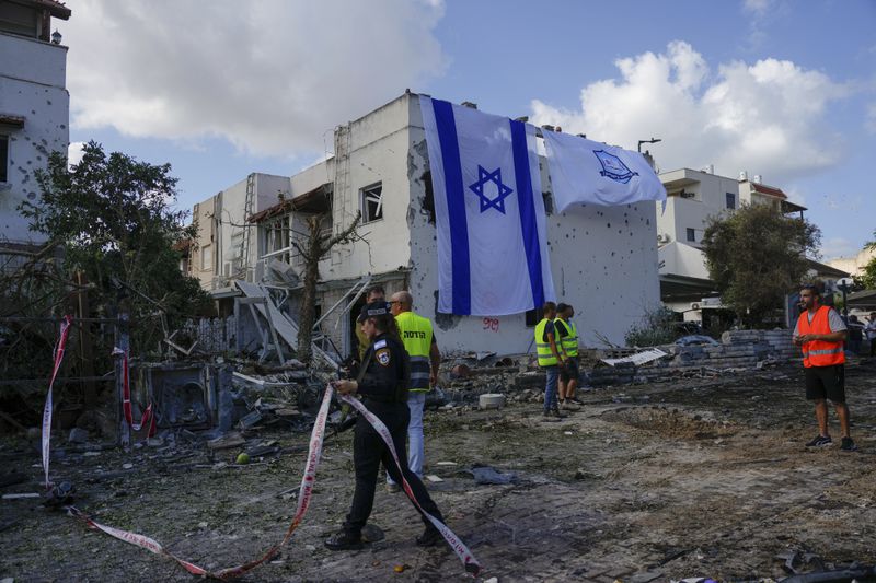 Municipality workers hang an Israeli flag over a damaged building that was hit by a rocket fired from Lebanon, in Kiryat Bialik, northern Israel, on Sunday, Sept. 22, 2024. (AP Photo//Ariel Schalit)