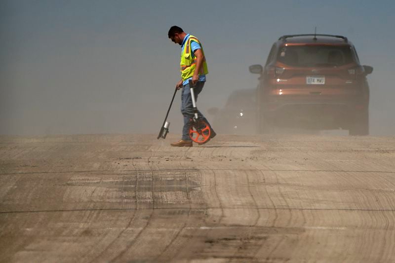 A worker is diffused by heat vapors while marking pavement on a street construction project as temperatures topped 100 degrees Fahrenheit (37.8 Celsius) on Monday, Aug. 26, 2024, in Lenexa, Kan. (AP Photo/Charlie Riedel)