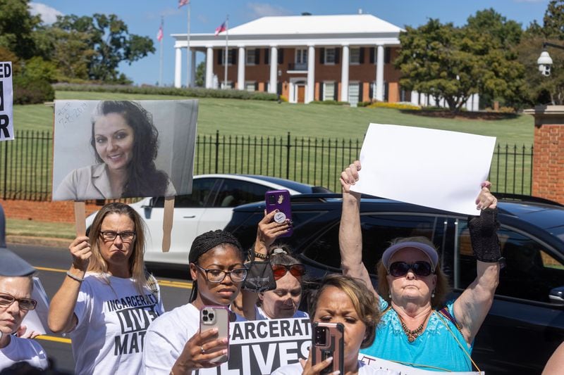 Brandie Widener (left) holds up a photograph of her sister Stephanie, who died in prison in 2019, while protesting across the street from the governor's mansion Tuesday, October 3, 2023. (Steve Schaefer/steve.schaefer@ajc.com)