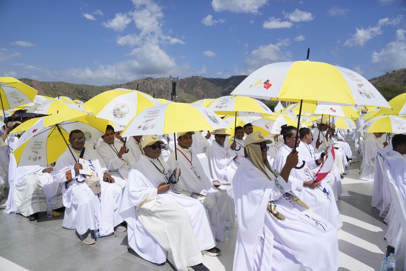 Faithful and priests use umbrellas with the colors of the Vatican flag to shield themselves from the sun as they wait for a mass presided over by Pope Francis to start in Tacitolu, some 8 kilometers west of Dili, East Timor, Tuesday, Sept. 10, 2024. Pope Francis presides over a mass in a seaside park on the same field where St. John Paul II celebrated an historic liturgy during East Timor's fight for independence from Indonesian rule. (AP Photo/Gregorio Borgia)