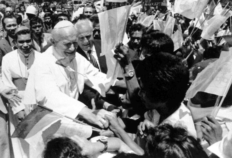 This Oct. 12, 1989 file photo shows Pope John Paul II shaking hands with flag-waving local students upon his arrival in Dili, East Timor. Pope Francis will clock 32,814 kilometers by air during the Sept. 2-13 visit to Indonesia, Papua New Guinea, East Timor, and Singapore, far surpassing any of his previous trips and notching one of the longest papal trips ever, both in terms of days on the road and distances traveled. (AP Photo/Bullit Marquez)