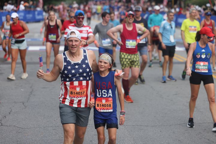 Scott Woodward and Lawson Woodward cross the finish line at the finish of the 55th running of the Atlanta Journal-Constitution Peachtree Road Race in Atlanta on Thursday, July 4, 2024.   (Jason Getz / AJC)