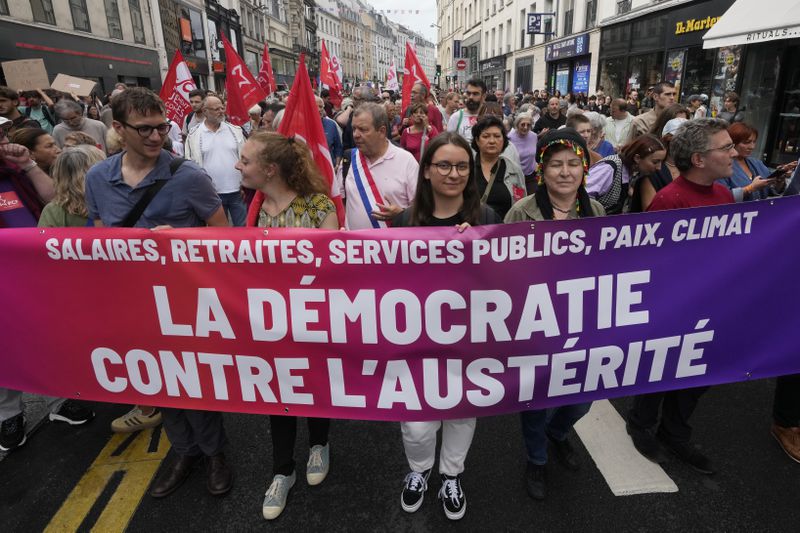 Demonstrators display a banner which reads 'democracy against austerity' during a protest, responding to a call from the far-left party who criticized as a power grab the president's appointment of a conservative new prime minister, Michel Barnier, in Paris, France, Saturday, Sept. 7, 2024. (AP Photo/Michel Euler)