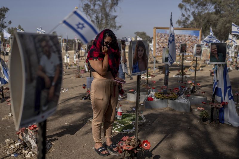 A woman stands next to photos of people killed and taken captive by Hamas militants during their violent rampage through the Nova music festival in southern Israel, which are displayed at the site of the event to commemorate the Oct. 7, massacre near Kibbutz Re'im on Thursday, June 20, 2024. A new kind of tourism has emerged in Israel in the months since Hamas’ Oct. 7 attack. For celebrities, politicians, influencers and others, no trip is complete without a somber visit to the devastated south that absorbed the brunt of the assault near the border with Gaza. (AP Photo/Ohad Zwigenberg)