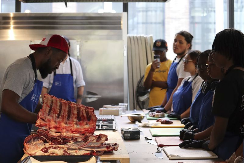 Abou Sow, the owner of Prince Abou's Butchery in Queens, shows students from George Westinghouse Career and Technical Education High School how to separate short rib from rib eye at Essex Kitchen in New York, May 21, 2024. (AP Photo/James Pollard)