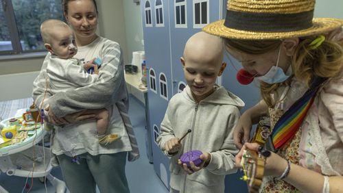 Tetiana Nosova, who goes by the clown name of Zhuzha, a volunteer from the "Bureau of Smiles and Support" plays a ukulele as she stands with Michael Bilyk, who is held by his mother Antonina Malyshko, and Kira Vertetska, 8, at Okhmatdyt children's hospital in Kyiv, Ukraine, Thursday Sept. 19, 2024. (AP Photo/Anton Shtuka)