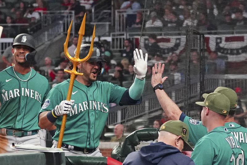 Seattle Mariners' Eugenio Suarez, second from left, holds a trident as he is greeted at the dugout after hitting a two-run home run in the seventh inning of a baseball game against the Atlanta Braves , Saturday, May 20, 2023, in Atlanta. (AP Photo/John Bazemore)