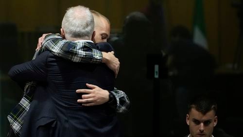 Ethan Elder, left, back to camera, father of Finnegan Lee Elder, hugs his son before the reading of the judgment at the end of a hearing for the appeals trial in which Finnegan is facing murder charges for killing Italian Carabinieri paramilitary police officer Mario Cerciello Rega, in Rome, Wednesday, July 3, 2024. At right sits Gabriel Natale Hjorth charged for the same killing. (AP Photo/ Alessandra Tarantino)