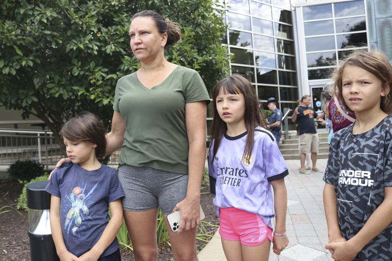 Lisa Czawlytko, second from left, describes a house explosion near her home as feeling like like an earthquake on Sunday, Aug. 3, 2024 in Bel Air, Md. She said it woke her and her three children up Sunday morning and knocked aluminum siding from the roofs of four nearby buildings. (AP Photo/Brian Witte)