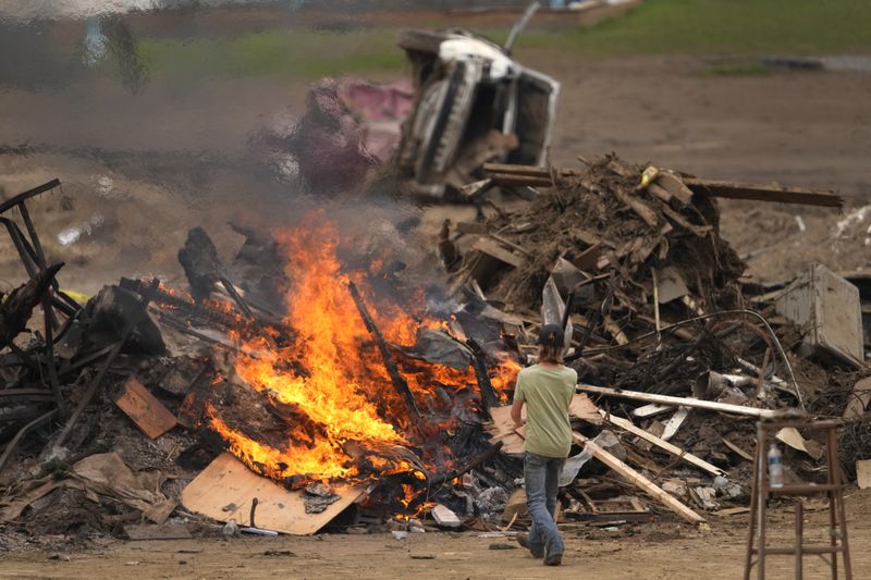 A person throws objects on a burning debris pile in the aftermath of Hurricane Helene, Friday, Oct. 4, 2024, in Erwin, Tenn. (AP Photo/Jeff Roberson)