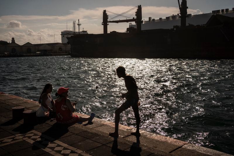 Rafael Murillo, a young diver who performs shows in the sea for tips, chats with two women resting along the water to cool off from the heat in Veracruz, Mexico, on June 15, 2024. Human-caused climate change intensified and made far more likely this month's killer heat with triple digit temperatures, a new flash study found Thursday, June 20. (AP Photo/Felix Marquez)