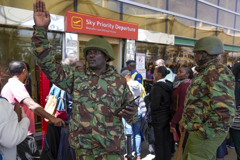 A Kenyan police officer gestures as stranded passengers wait for their delayed flights out of JKIA airport after flights were grounded following workers’ protesting a planned deal between the government and a foreign investor, in Nairobi, Kenya, Wednesday, Sept. 11, 2024. (AP Photo/Brian Inganga)