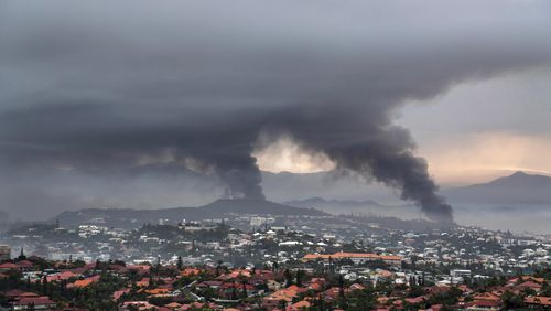 FILE - Smoke rises during protests in Noumea, New Caledonia, Wednesday May 15, 2024. The French Pacific territory of New Caledonia is shortening its overnight curfew and reopening its international airport that was closed to commercial flights for more than a month because of deadly violence. The archipelago's high commissioner said Sunday, June 16, 2024 the La Tontouta airport that links New Caledonia’s capital, Nouméa, to Sydney, Tokyo and other Pacific hubs will reopen Monday. (AP Photo/Nicolas Job, File)
