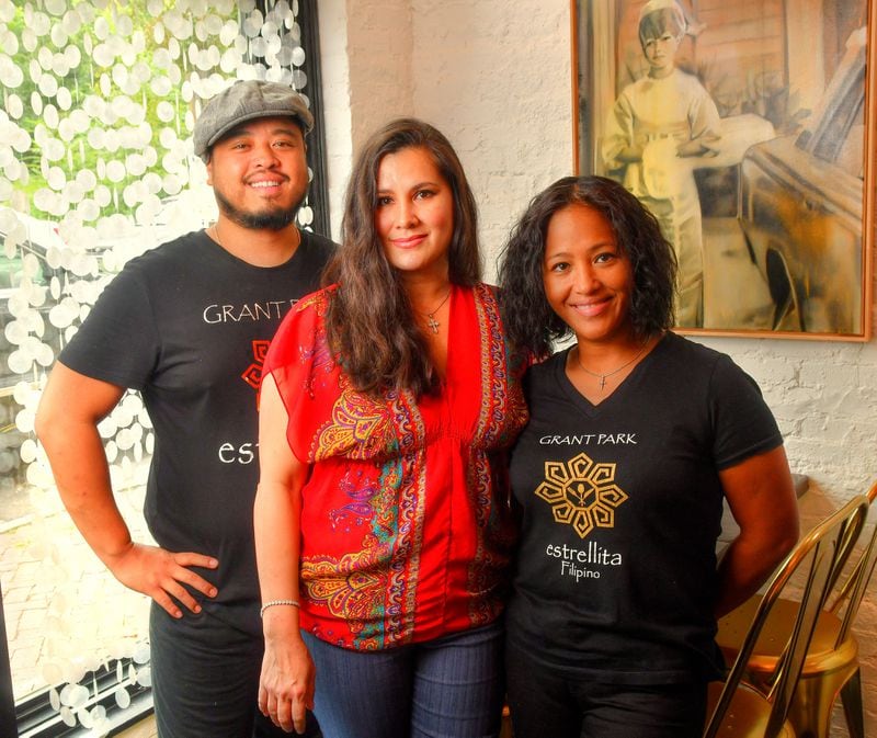 Executive chef Walter Cortado (left) and Hope Webb (center), co-owners of Estrellita restaurant in Grant Park, and chef Blesseda Gamble, Cortado's sister, pose in the restaurant's dining area. The window decorations (left) called Kapis (oyster shells strung together) were made by Webb and are traditional Filipino curtains, or room dividers. The painting (right) by artist Laura Bochet is painted from a photo of Hope Webb's mother Estrella. Chris Hunt for The Atlanta Journal-Constitution