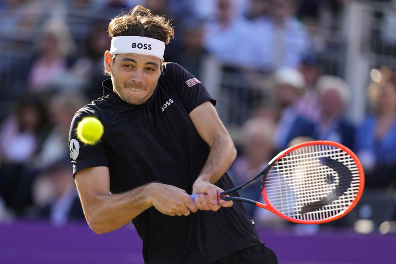 Taylor Fritz of the US plays a return to Milos Raonic of Canada during their men's singles match on day five of The Queen's Club tennis tournament, in London, Wednesday, June 19, 2024. (AP Photo/Kirsty Wigglesworth)
