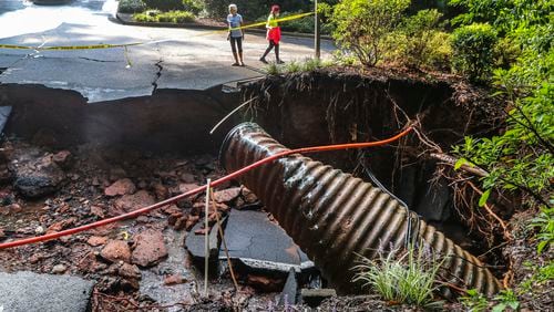 Onlookers overlook the road that was washed away at Fawn Place at East Lake Parkway in Marietta on Wednesday, Sept. 8, 2021, after torrential downpours of rain overnight brought flooding and damage to the Cobb County area. Public sector staffing challenges have strangled the government's response to infrastructure repairs across the county.  (John Spink / John.Spink@ajc.com)