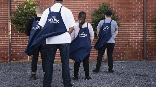 Four members of the Giving Kitchen staff are pictured facing away from the camera, wearing their aprons like capes.