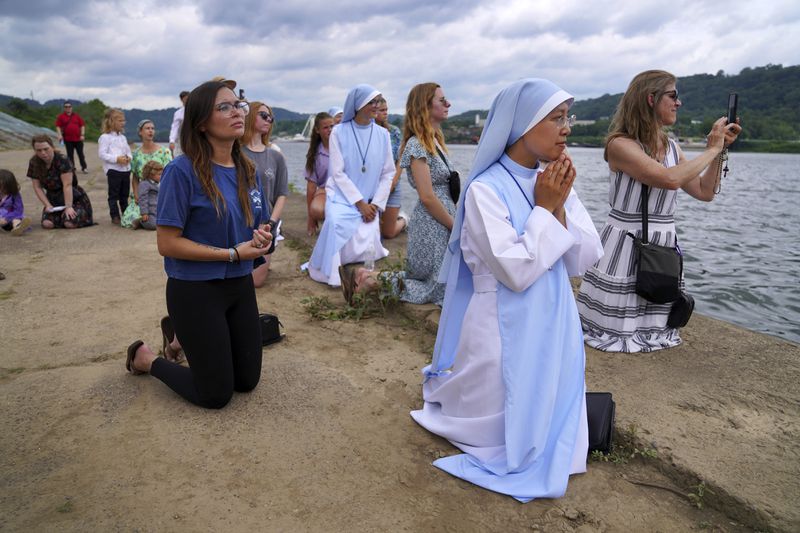 Sister Mary Fatima Pham, second from right, kneels with her fellow Catholics as they watch the Eucharist brought on board a boat on the Ohio River at the Steubenville Marina in Steubenville, Ohio, Sunday, June 23, 2024. The National Eucharistic Pilgrimage will conclude at the National Eucharistic Congress in Indianapolis in mid-July, the first held in more than 80 years. (AP Photo/Jessie Wardarski)