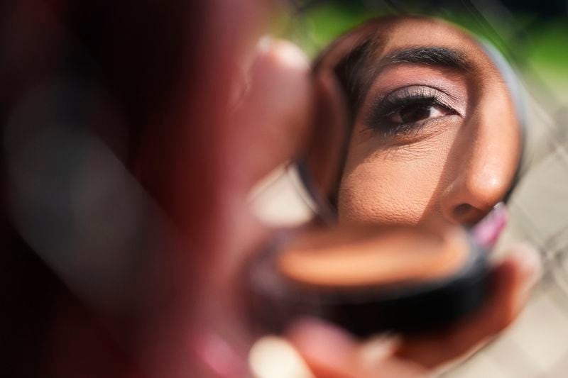 Julieth Luna Garcia, a transgender woman from El Salvador, looks into a compact mirror at Horner Park in Chicago, Monday, Sept. 30, 2024. (AP Photo/Nam Y. Huh)