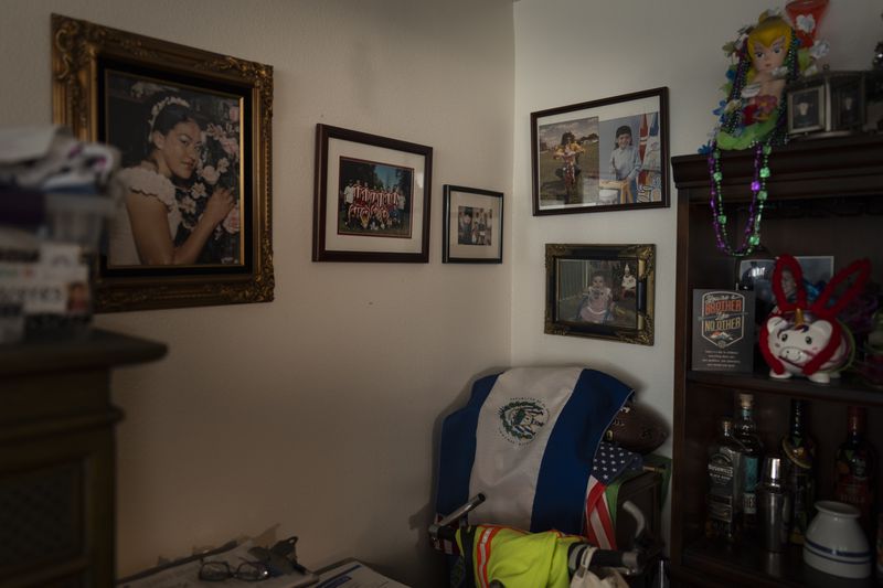 A wall in Marina Maalouf's apartment is adorned with family photos as an El Salvadoran flag is draped over an American flag in Los Angeles, Tuesday, Oct. 1, 2024. (AP Photo/Jae C. Hong)