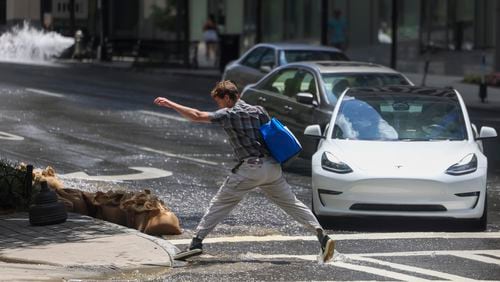 A man leaps to jump over water spilled from a fire hydrant spilled up West Peachtree Street as he crosses 14th street, Monday, June 3, 2024, in Atlanta. (Jason Getz / AJC)
