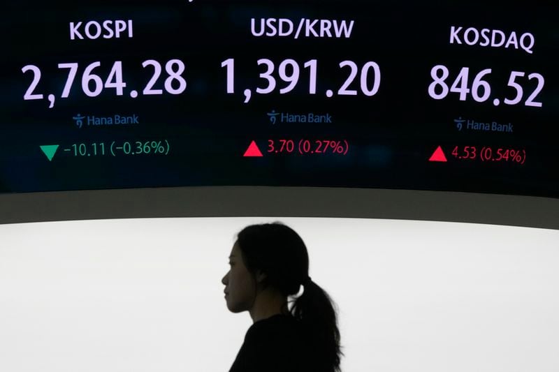A currency trader passes under the screen showing the Korea Composite Stock Price Index (KOSPI), top left, and the foreign exchange rate between U.S. dollar and South Korean won, top center, at the foreign exchange dealing room of the KEB Hana Bank headquarters in Seoul, South Korea, Wednesday, June 26, 2024. (AP Photo/Ahn Young-joon)