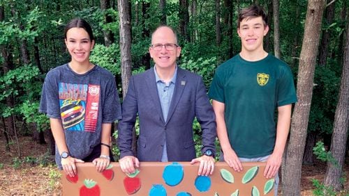 Faustina Barcena (left) stands with Adam Pomeranz, president and CEO of Annandale Village (center), and her brother, John, in front of a bench she created for the Suwanee assisted living facility. Courtesy