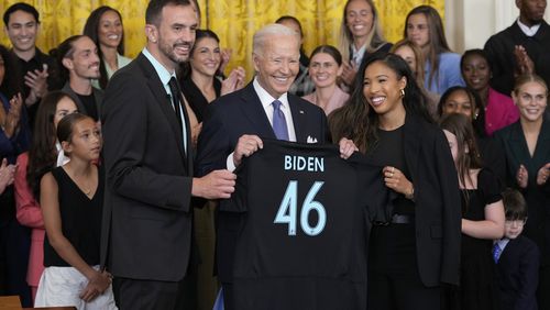 President Joe Biden, center, is presented with a team jersey from NJ/NY Gotham FC head coach Juan Carlos Amoros, left, and teammate Midge Purse, right, during an event in the East Room of the White House in Washington, Monday, Sept. 23, 2024, to welcome the NJ/NY Gotham FC and celebrate their 2023 NWSL championship. (AP Photo/Susan Walsh)