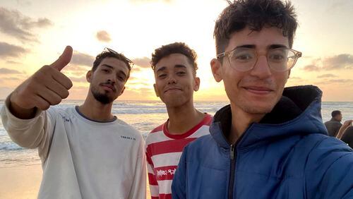 In this undated photo provided by Helmi Hirez, Mohamed (Medo) Halimy, left, and twin brothers Mohammed Hirez, center, and Helmi Hirez, right, stand on a beach in Gaza. (Helmi Hirez via AP).