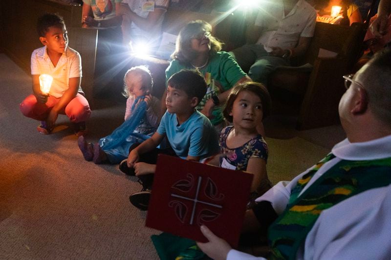 Children hold candles as Rev. Jennifer Roberts (off screen) reads a children book based on a Dolly Parton song as Rev. Matthew D. O'Rear sits along with them during the Drag Me to Church event at St. Luke Lutheran on Sunday, 25, 2023 in Atlanta. (Michael Blackshire/Michael.blackshire@ajc.com)