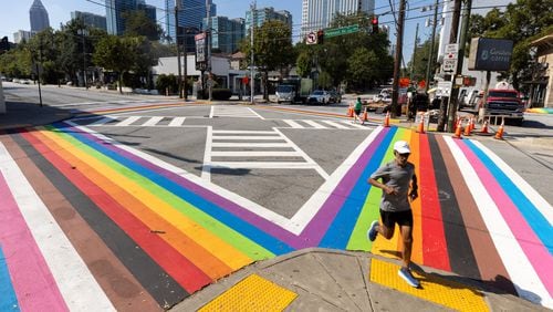 A runner crosses the rainbow crosswalk in Midtown Atlanta on Monday, Oct. 7, 2024. The crosswalk got an inclusive makeover with black and brown stripes to represent communities of color and to showcase the colors of the transgender flag. (Arvin Temkar / AJC)