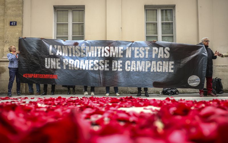 Anti far-left protesters display a banner that reads, "antisemitism is not a campaign promise" next to the entrance where the media conference will take place of the leaders of France left-wing parties for the upcoming election in Paris, Friday, June 14, 2024. Leaders of France's left-wing parties, allied in a coalition known as the New Popular Front on Friday outlined their plan to fend off the far-right from claiming power at the upcoming snap national election. (AP Photo/Thomas Padilla)