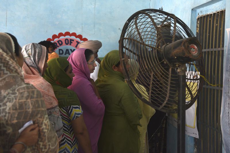 FILE - Women wait in a queue to cast their vote standing in front of a fan at a polling booth on a hot summer day during the seventh and the last phase of the general election, near Amritsar, India, Saturday, June 1, 2024. The official number of heat deaths listed in government reports barely scratches the surface of the true toll and that's affecting future preparations for similar swelters, according to public health experts. (AP Photo/Prabhjot Gill, File)